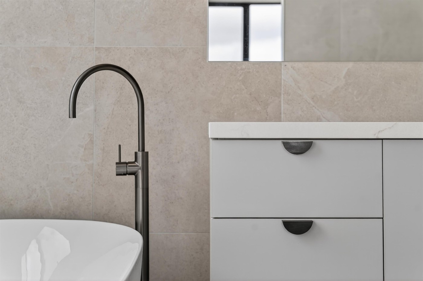 Bathroom with a matte black freestanding tap, stone tiles and white joinery in a Varcon custom home