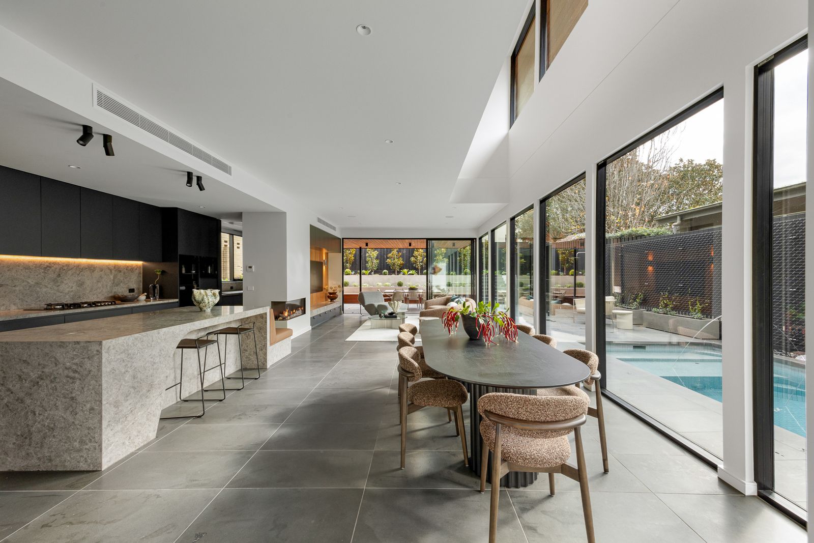 Open-plan kitchen and dining at The Ora with floor-to-ceiling glazing overlooking the pool